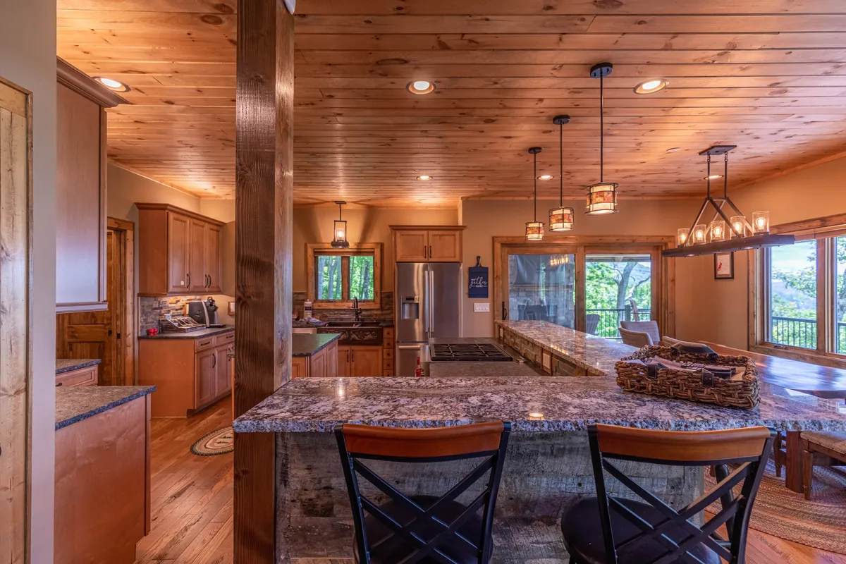 A gourmet kitchen featuring a large island with bar stools, granite countertops, pendant lighting, and expansive windows that offer scenic mountain views. The setting is ideal for cooking, gathering, and enjoying the landscape beyond.