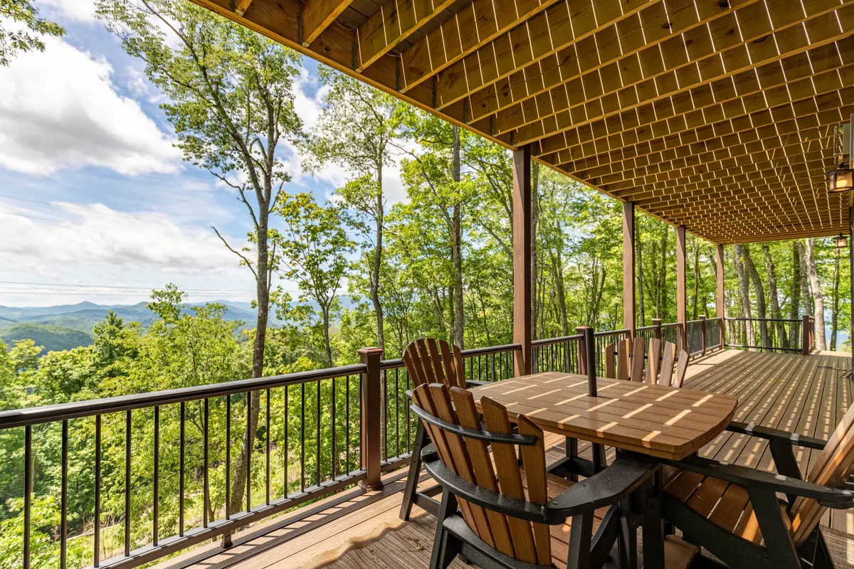 A beautifully set wooden deck features a dining table facing a sweeping view of mountains. The space invites outdoor dining, social gatherings, and tranquil appreciation of the surrounding landscape.