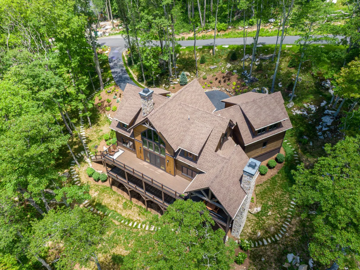 A spacious wooden deck with a stone chimney, large windows, and surrounding greenery. The deck offers seating for outdoor gatherings, with views of the lush landscape and opportunities for stargazing or enjoying sunset moments together as a family.
