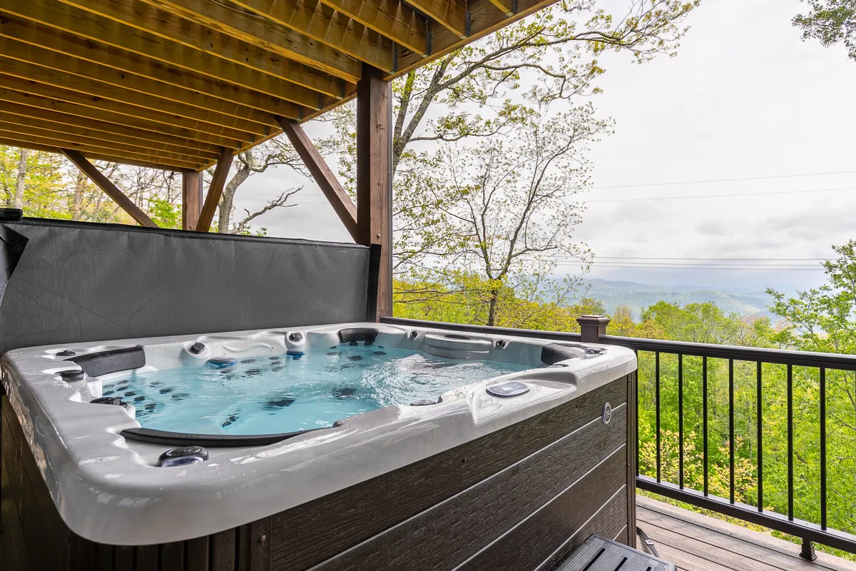 A secluded outdoor hot tub surrounded by tall trees and lush greenery, with a sweeping view over the Blue Ridge mountains. The tranquil setting invites relaxation, conversation, and stargazing, offering a peaceful retreat after days filled with adventure.