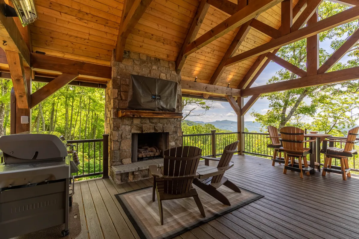 A cozy outdoor gathering spot featuring a stone fireplace, built-in grill, ample seating, and sweeping mountain vistas. Guests are seen socializing, barbecuing, and relaxing as the sun sets over the mountains, adding warmth and ambiance to the scene.