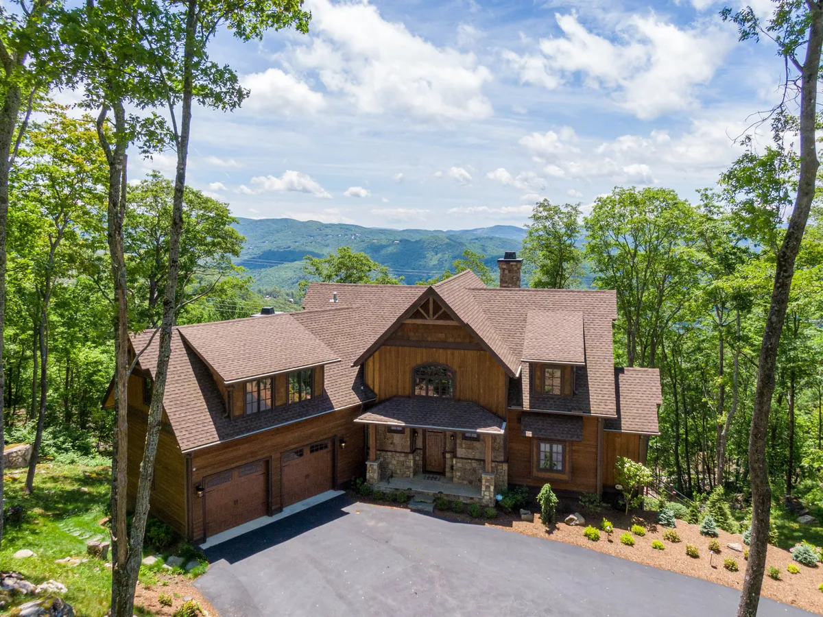 The image showcases a stunning mountain lodge with a wooden exterior and beautiful stone accents, nestled among tall trees with sweeping views of the mountains in the background. Bathed in tranquil natural light, the scene evokes a sense of peaceful seclusion and invites thoughts of relaxing outdoor gatherings or early morning hikes.