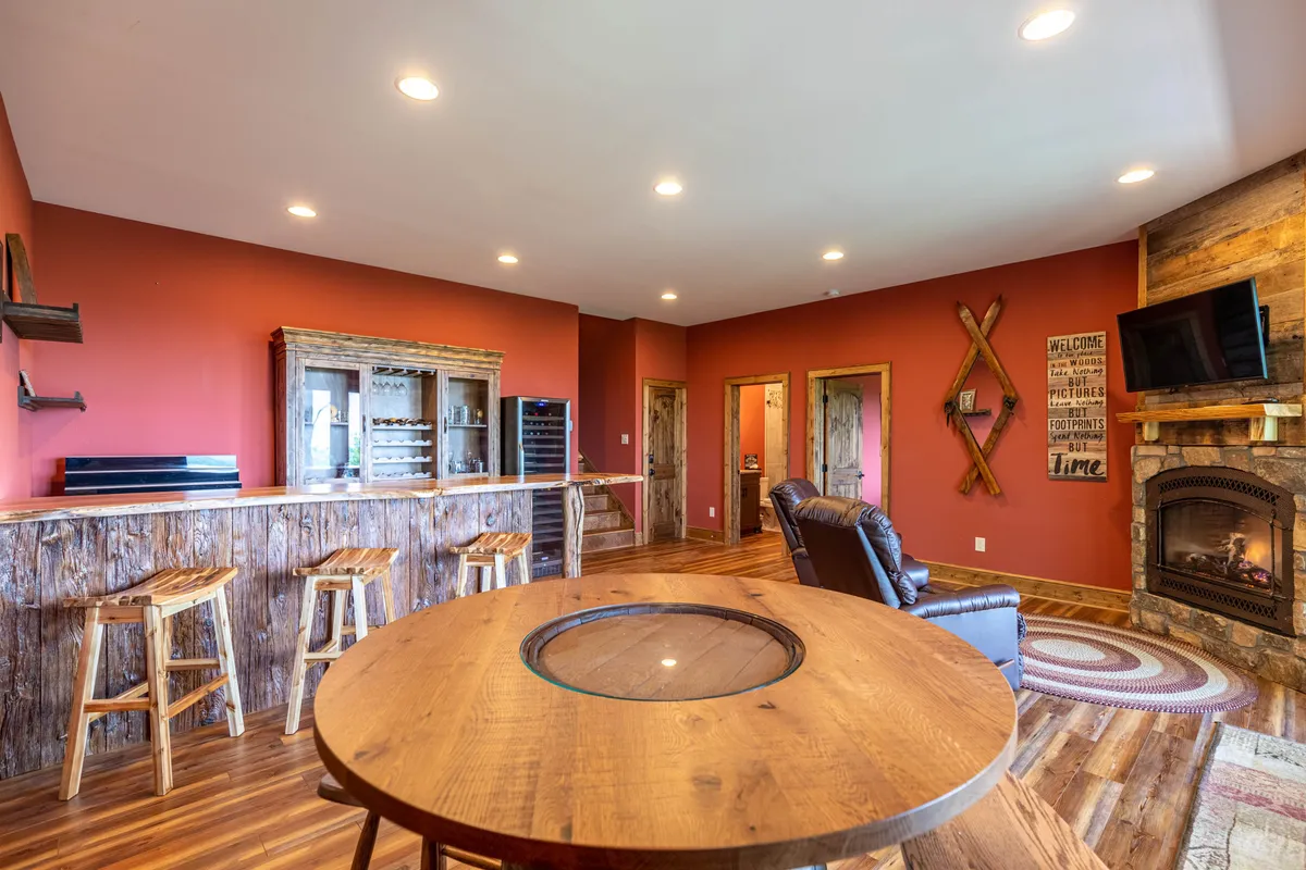 A cozy lounge area with a round wooden table, a custom bar, a fireplace, and a TV. The setting is perfect for relaxing with friends, enjoying a drink from the bar, or unwinding by the fire while watching TV.