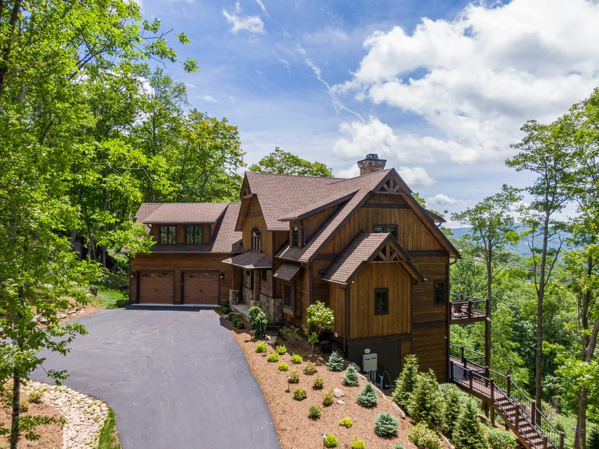 A welcoming view of the wooden exterior of the house, surrounded by landscaped gardens, a driveway leading to the garage, and abundant trees. The scene hints at proximity to trails and the seamless blend of comfort and nature.