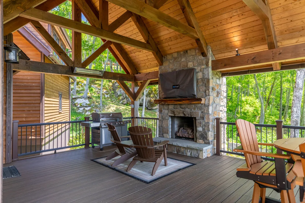 An inviting exterior setting with rustic wooden beams, a stone fireplace, grill, and Adirondack chairs arranged for outdoor dining and gatherings. The fire glows as friends and families share stories and meals by the grill under the open sky.