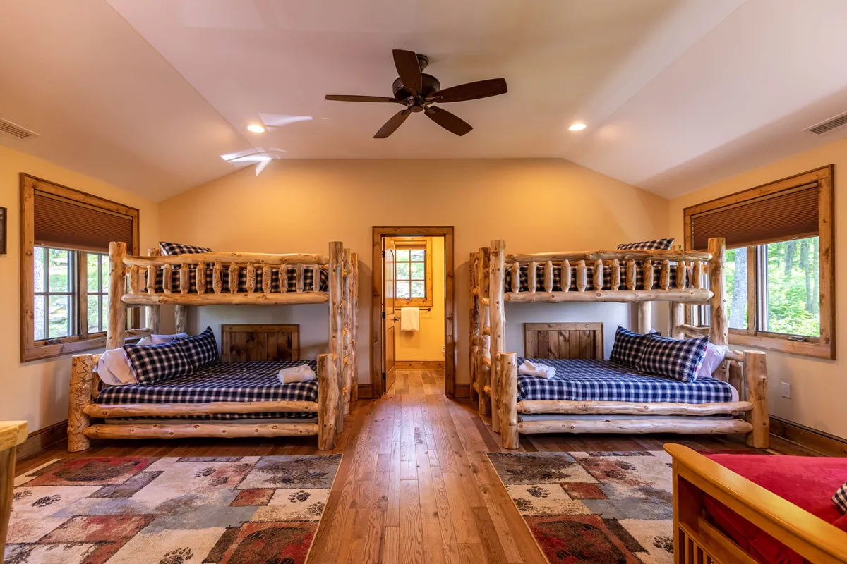 A cheerful bunk room with multiple bunk beds, large windows that allow sunlight to fill the room, and a soft area rug. The layout invites both restful sleep and playful group activities, making it ideal for children or group stays.